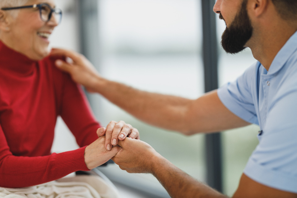 A caregiver holding a senior client's hand, both smiling